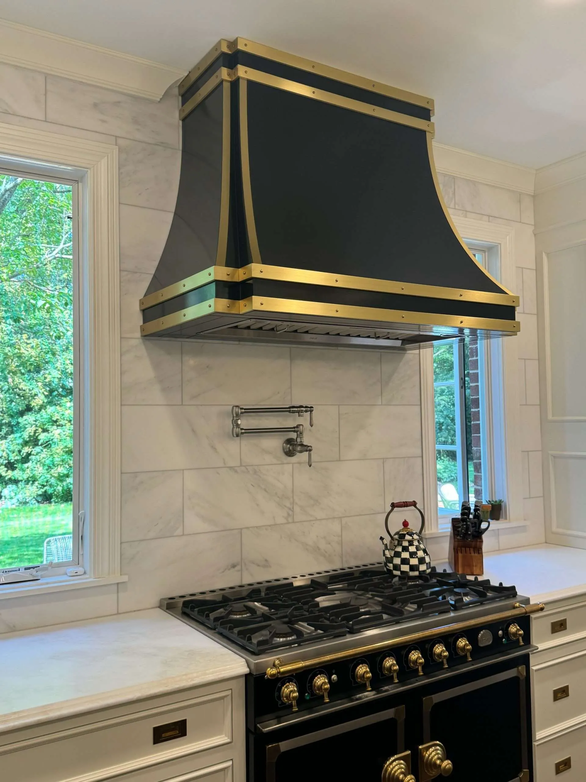 Darkened steel range hood with brass rivets over a large gas range