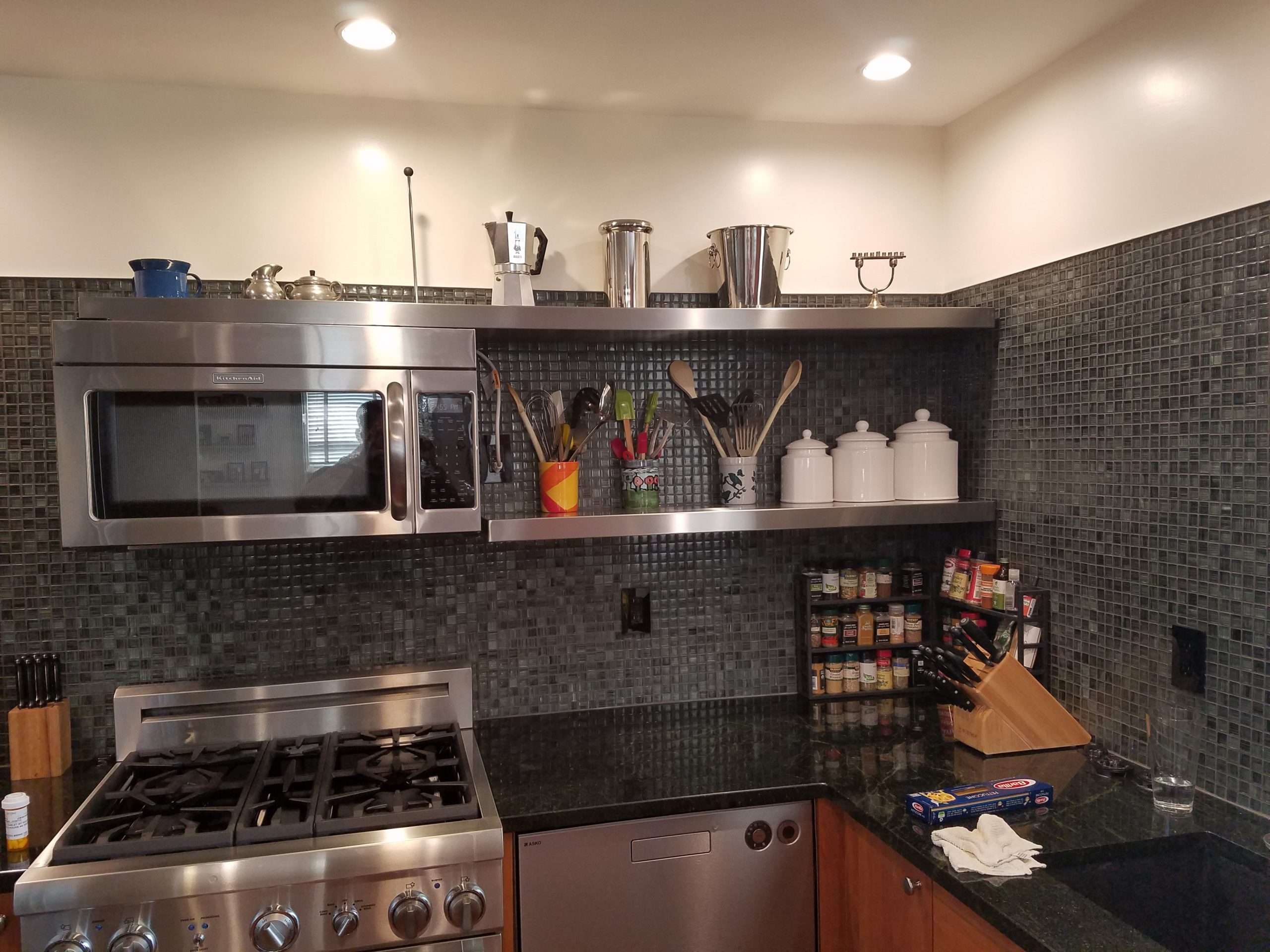 Stainless steel floating shelves above a kitchen range and backsplash, by Custom Metal Home