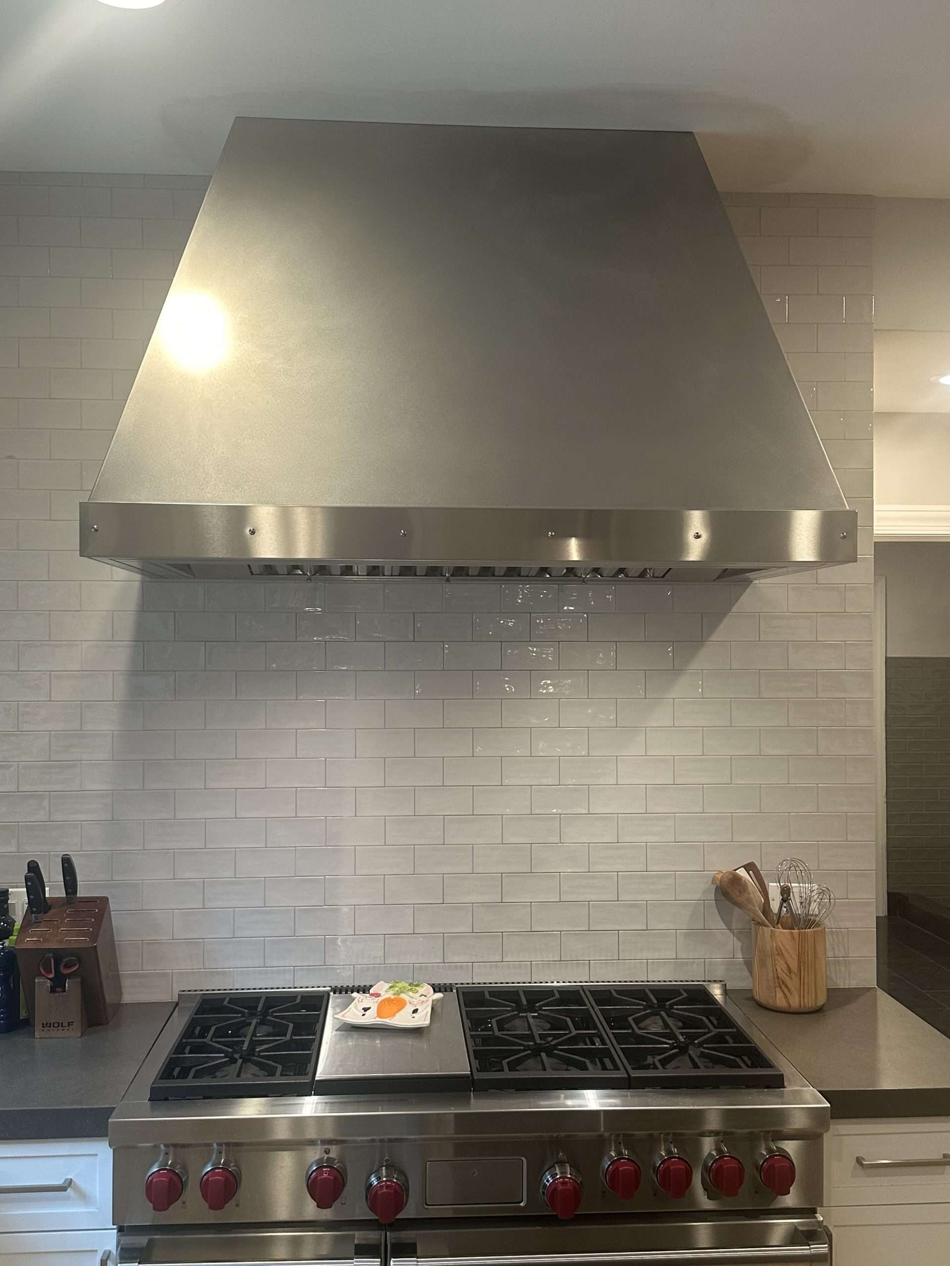 Stainless steel range hood with a matte finish over a professional range, by Custom Metal Home