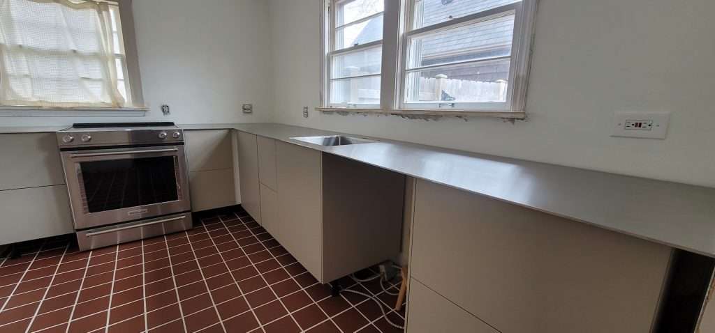 Custom stainless steel plate countertops installation in modern kitchen with stainless range and large window